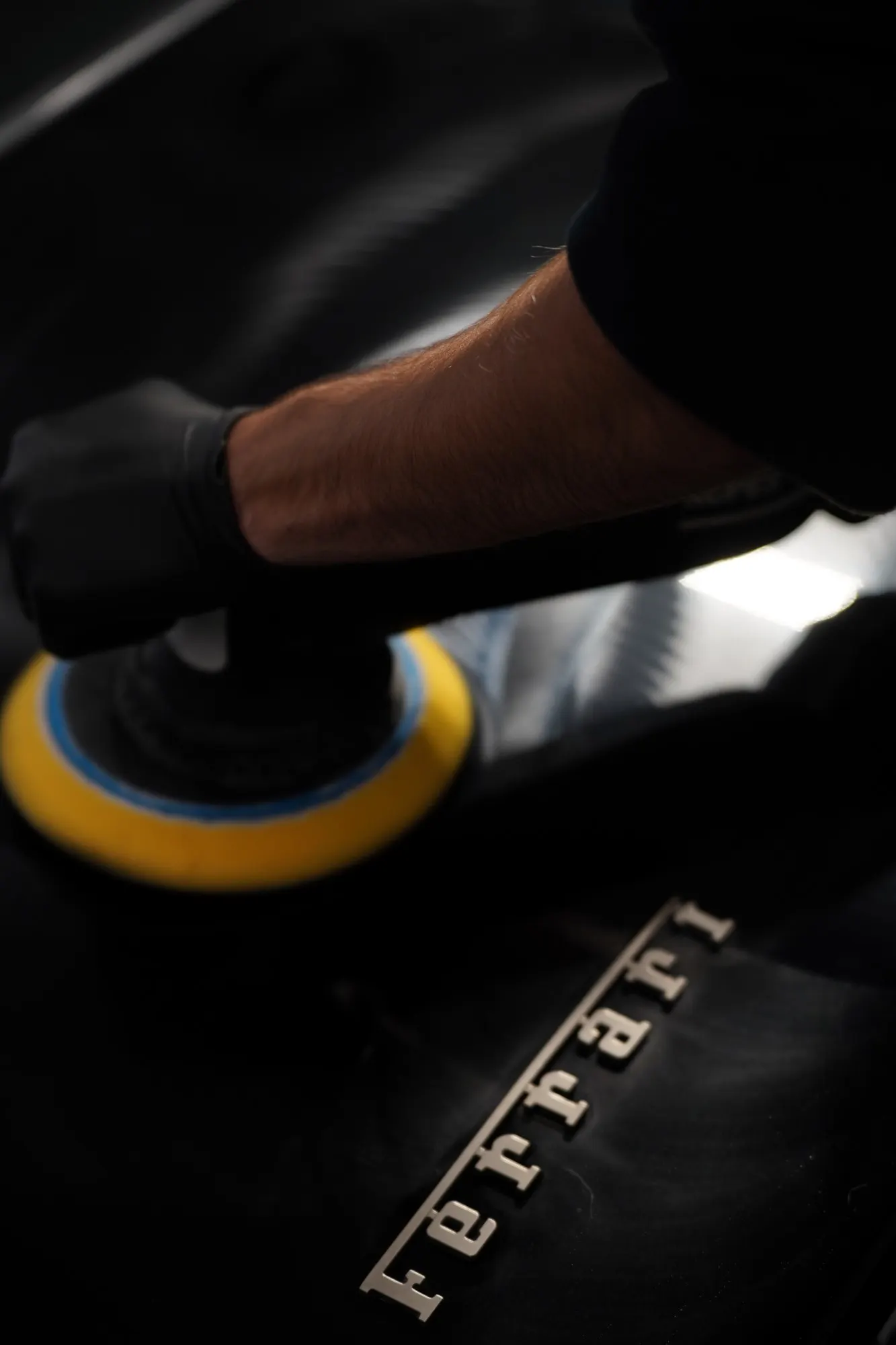 Machine-polishing the hood of a black Ferrari, badge catching the light